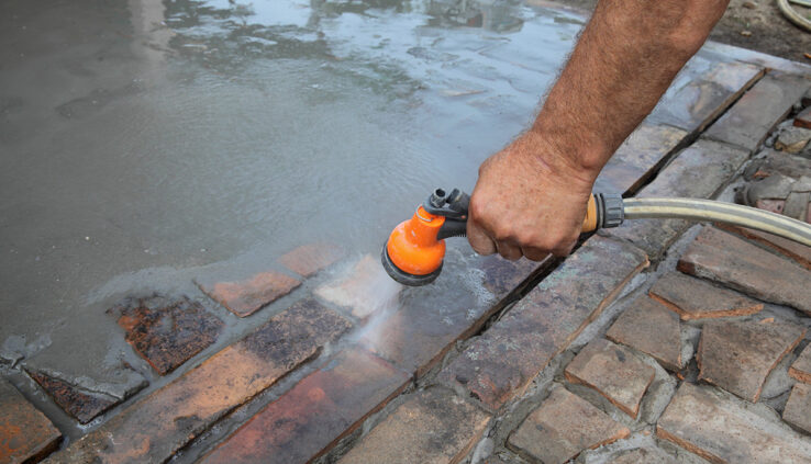 Cleaning concrete with a garden hose to remove excess dirt and debris.